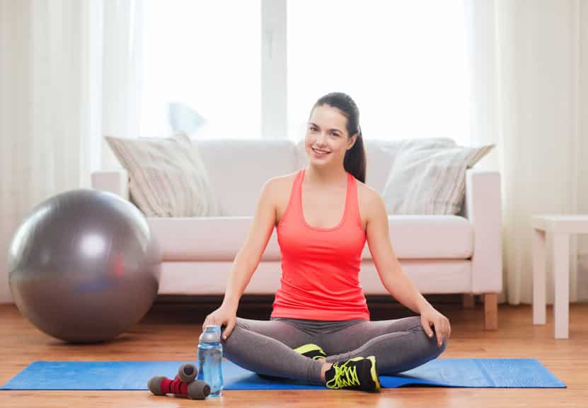 fitness, home and diet concept - smiling teenage girl sitting on mat with sports equipment at home