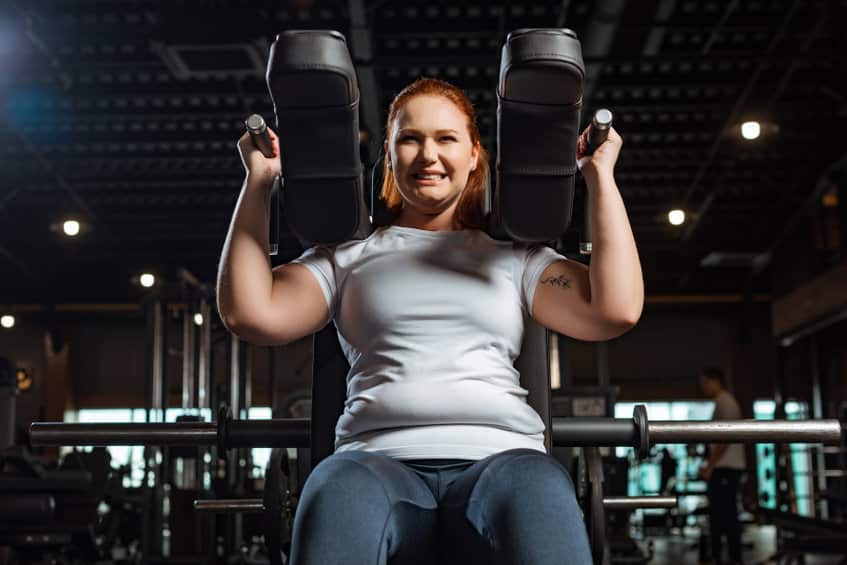 cropped view of purposeful overweight girl doing arms extension exercise on fitness machine