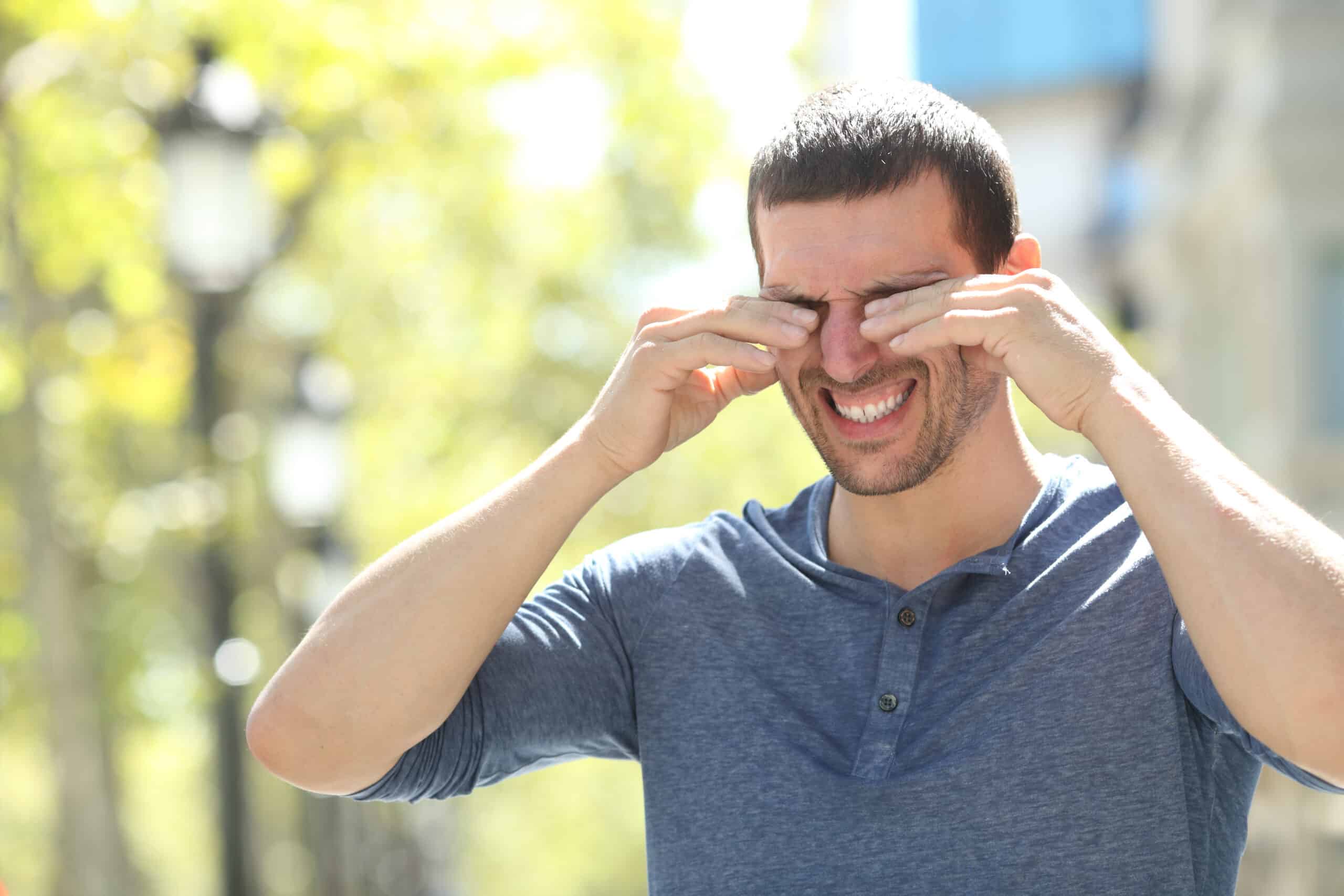 Adult man scratching itchy eyes in the street