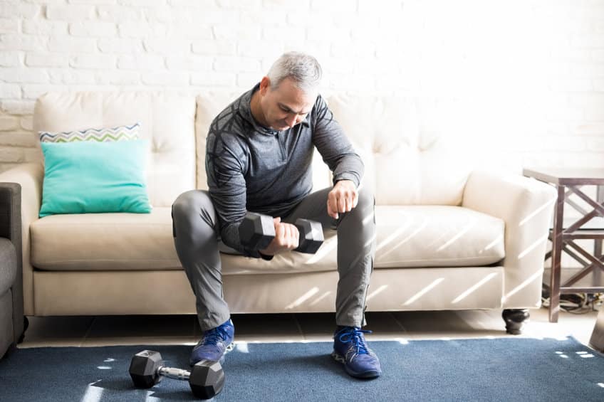 Middle aged man exercising with dumbbells at home