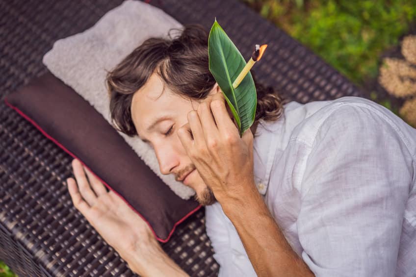 man having an ear candle therapy against the backdrop of a tropical garden