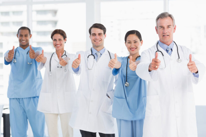 Group portrait of happy confident doctors gesturing thumbs up at hospital