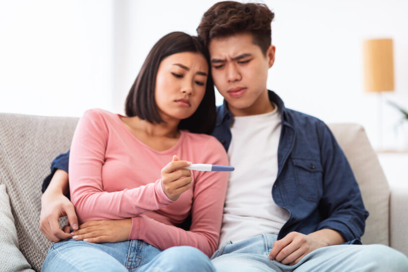 Frustrated Japanese Couple Holding Negative Pregnancy Test At Home