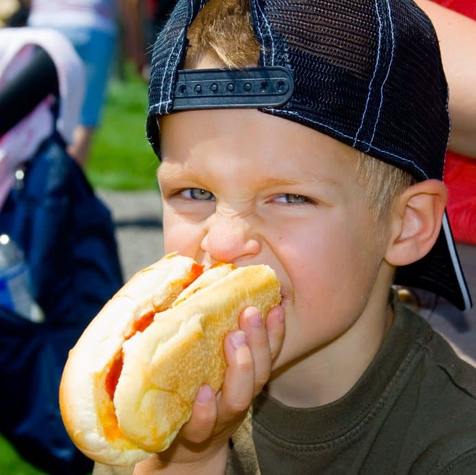 boy in baseball hat eating a hot dog